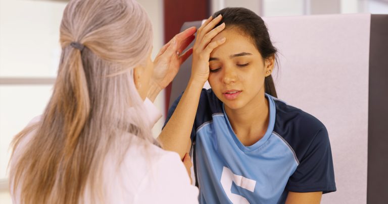 A young soccer player with a head injury recieves medical attention. An elderly doctor checks the young soccer player for a concussion