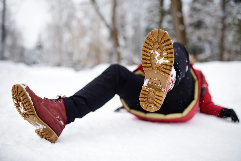Shot of person during falling in snowy winter park. Woman slip on the icy path, fell and lies.