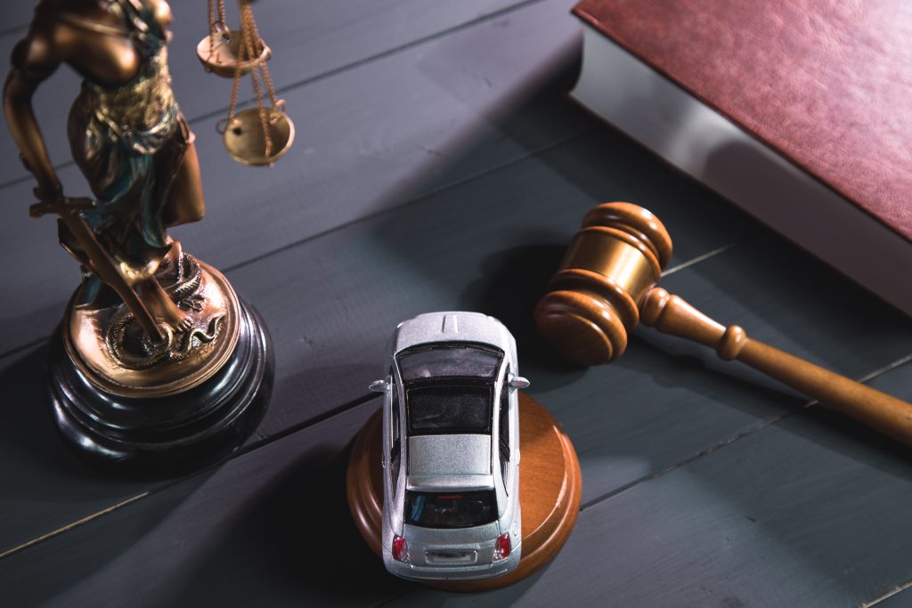 statue of justice, gavel and car on a wooden background.