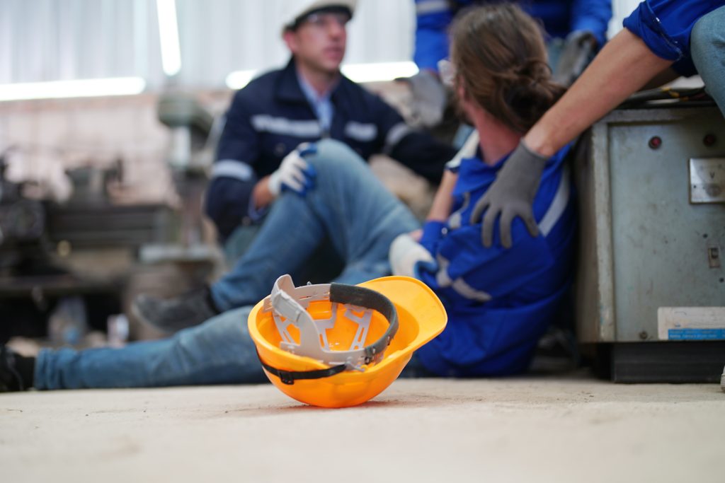Worker receiving industrial injury in factory and colleague helping him while injured on leg.