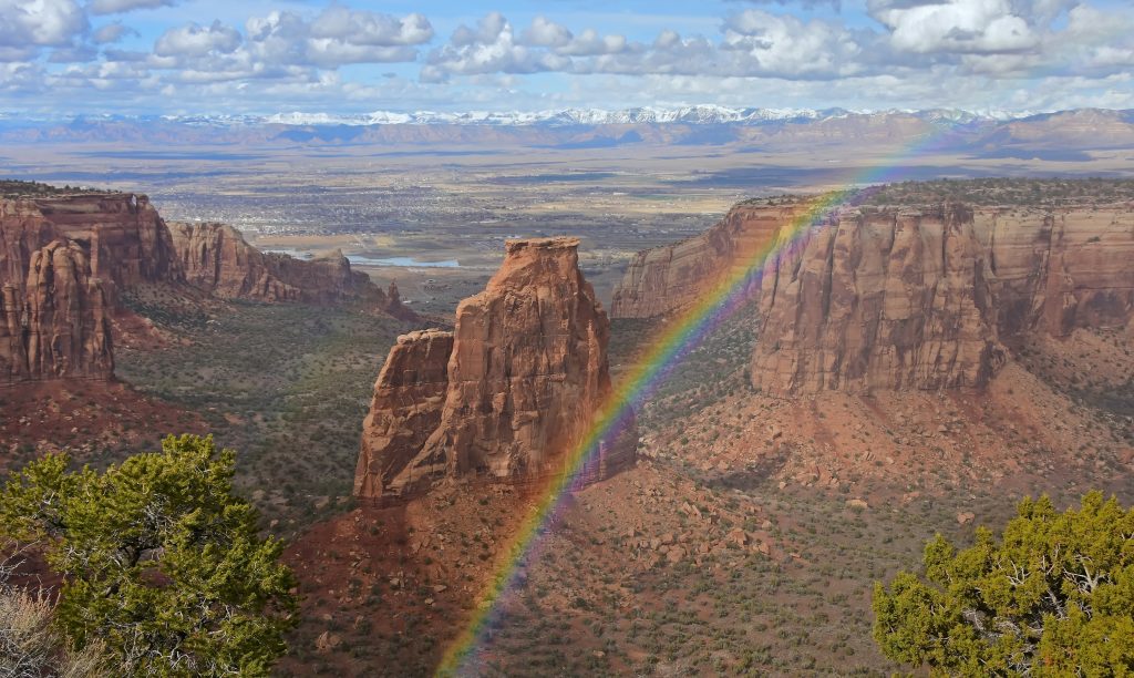 a dramatic rainbow on a sunny spring day over independence monument and the book cliffs in colorado national monument, fruita, colorado