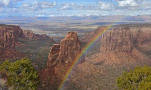 a dramatic rainbow on a sunny spring day over independence monument and the book cliffs in colorado national monument, fruita, colorado
