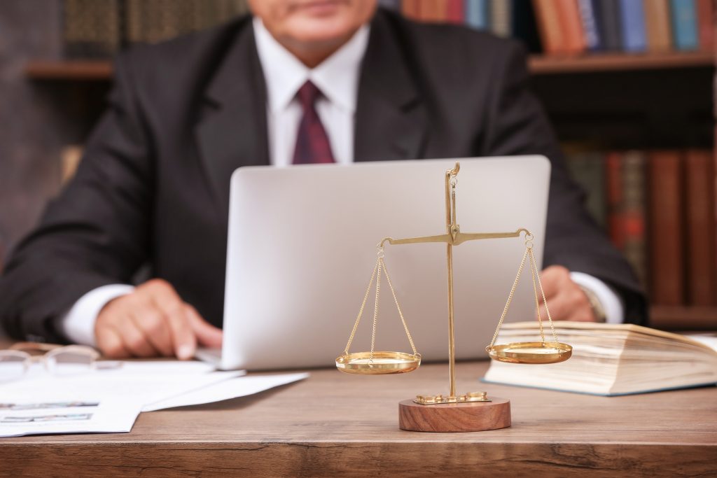 Scales of justice on wooden table and male lawyer on background